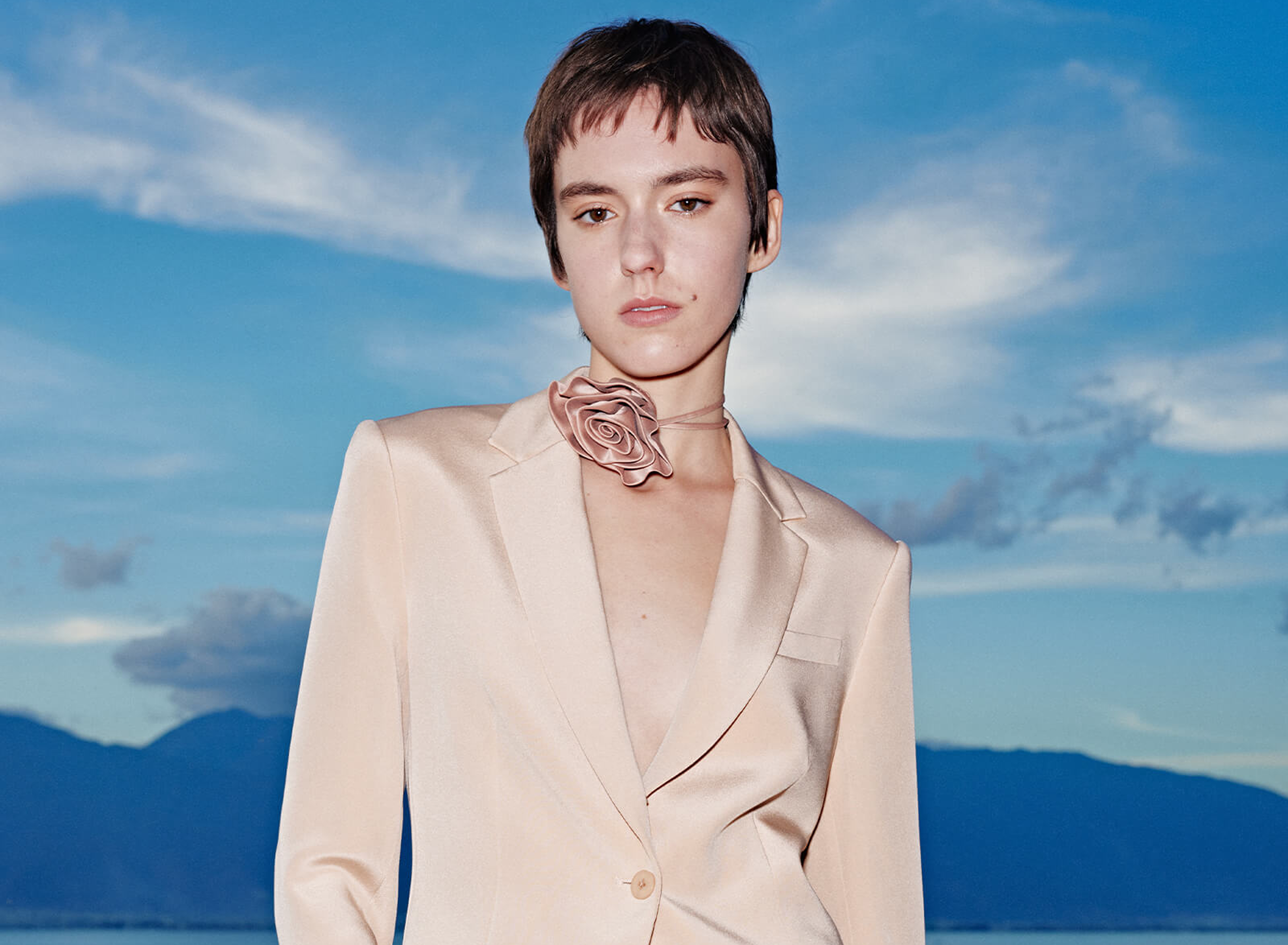 Person wearing beige blazer and rose choker outdoors