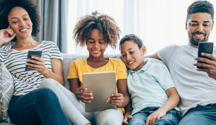 Family using tablets and smartphones together on couch