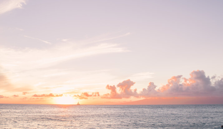 Sunset over calm ocean with sailboat and beach