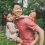 Father carrying smiling children outdoors in garden