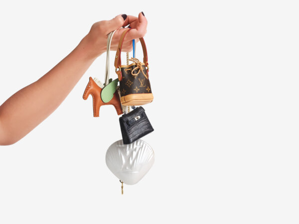 Hand holding four small luxury keychain bags of different shapes and designs against a white background.