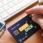 Hand holding cashback credit card near keyboard