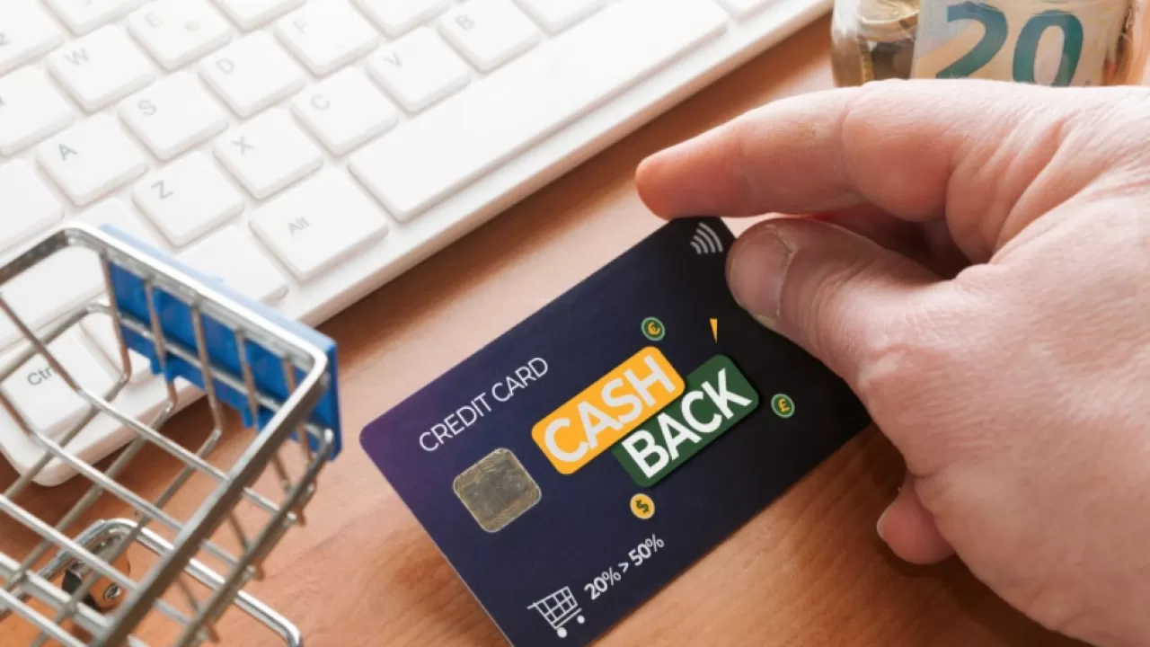 Hand holding cashback credit card near keyboard