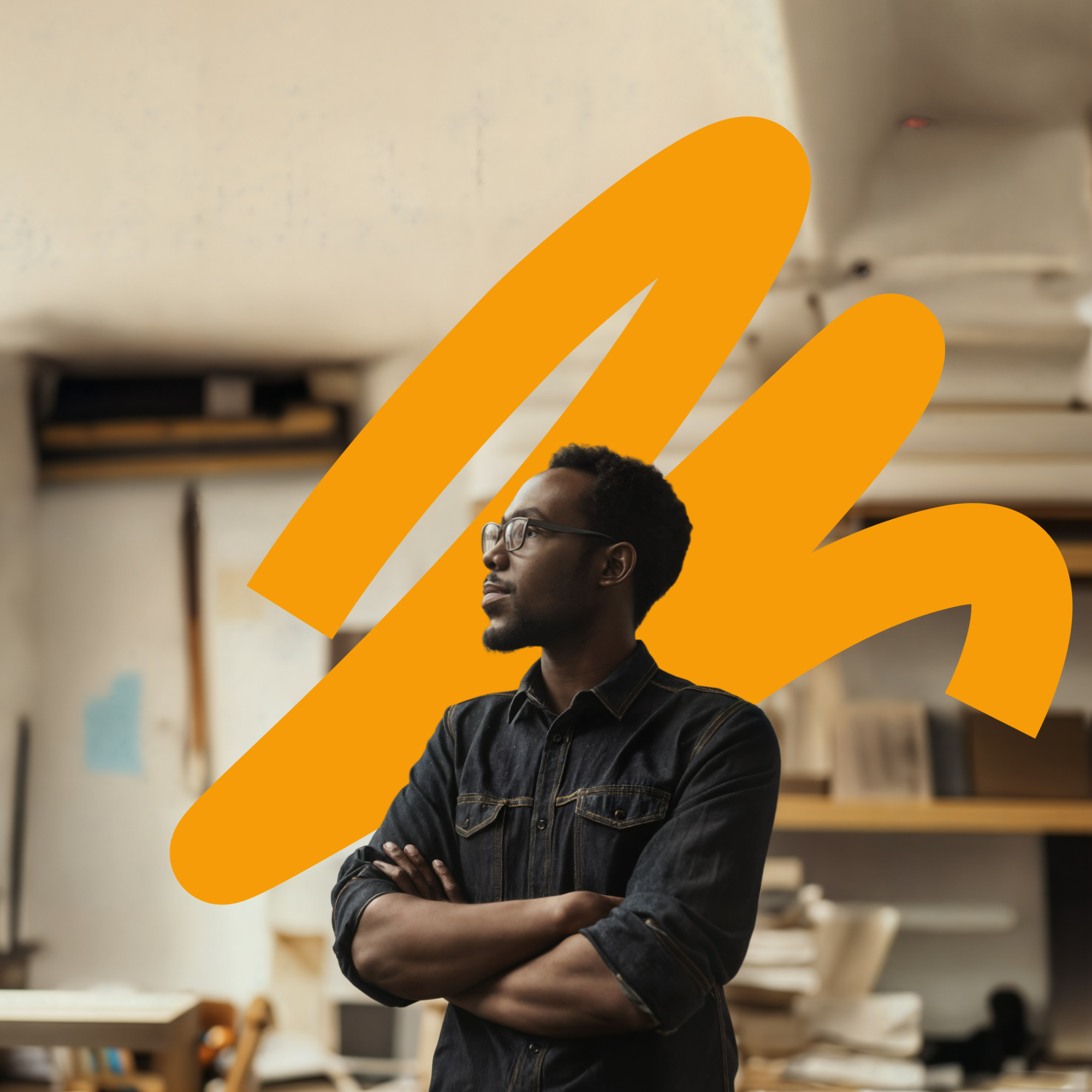 Man with glasses and a beard wearing a dark denim shirt standing with crossed arms in an indoor space with shelves and rolled-up papers, with an abstract orange shape overlay behind him