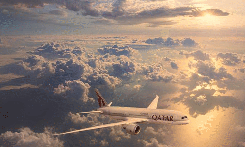 A Qatar Airways plane flying above clouds during a sunset with the sky lit in warm golden tones.
