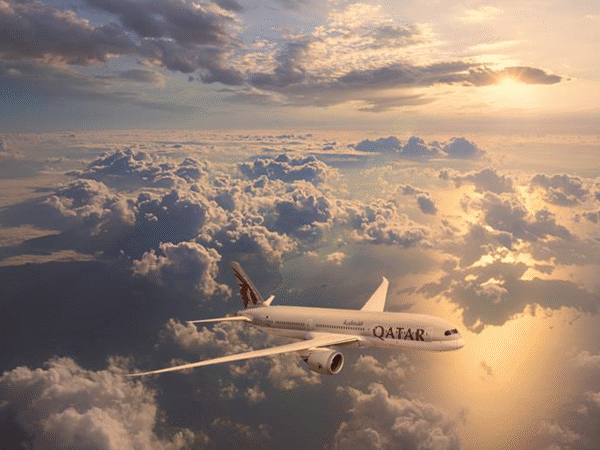 A Qatar Airways plane flying above clouds during a sunset with the sky lit in warm golden tones.
