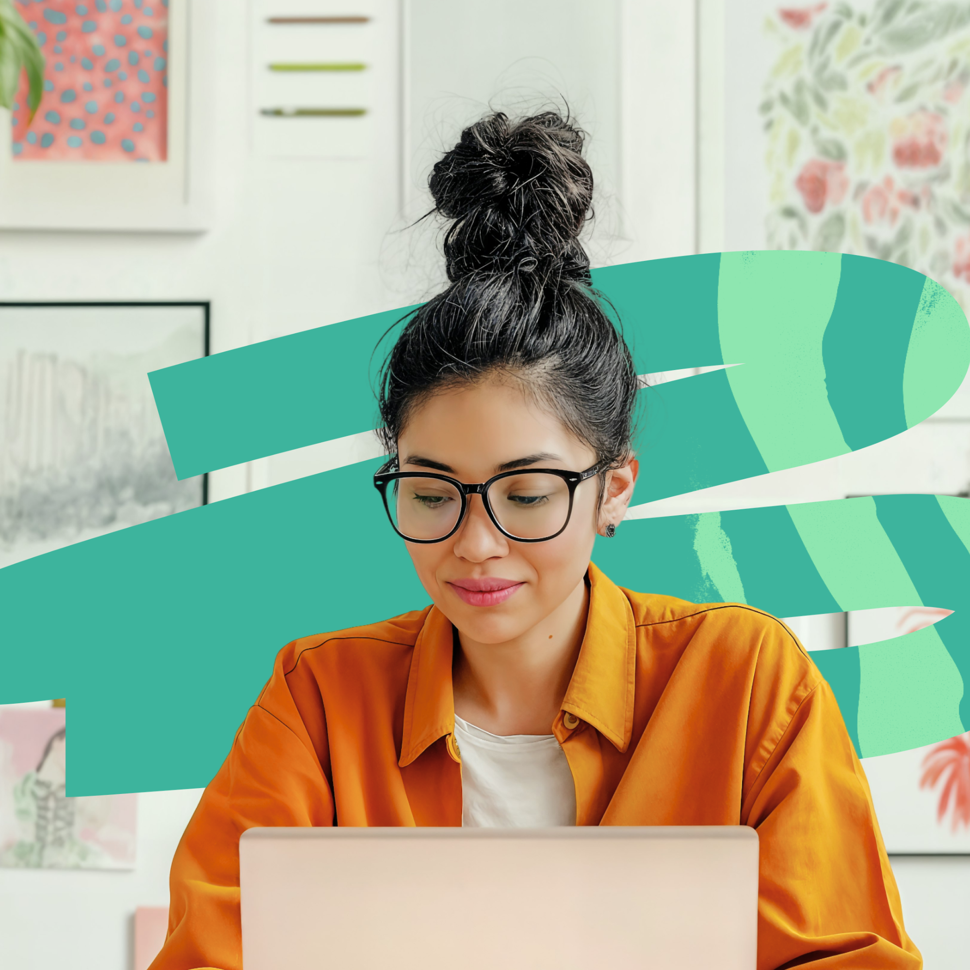 Young woman with black hair in a messy bun, wearing glasses and an orange shirt, working on a laptop with a colorful abstract green brushstroke and framed artwork in the background.