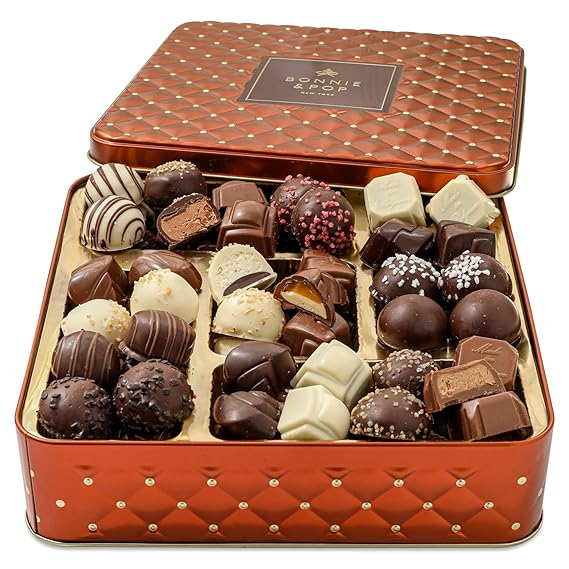 Open decorative metal tin containing an assortment of various chocolates including truffles, nut-covered pieces, and caramel-filled chocolates in white, milk, and dark varieties arranged in a gold tray