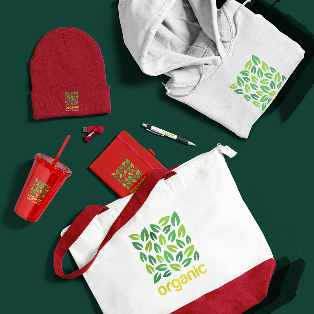 Collection of branded merchandise including a white and red tote bag, white hoodie, red beanie, red tumbler, red notebook, black and silver pen, and red USB drive, all featuring green leaf logos and the word 'organic' on a dark green background.