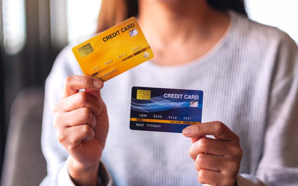 Person in a light-colored shirt holding a yellow credit card in the left hand and a blue credit card in the right hand