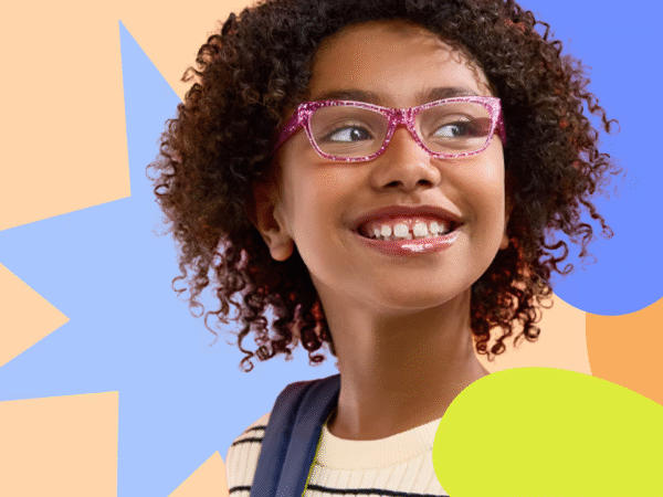 Young girl with curly hair wearing pink glasses and a striped shirt, smiling and looking to the side, against a colorful abstract background of star and flower shapes.
