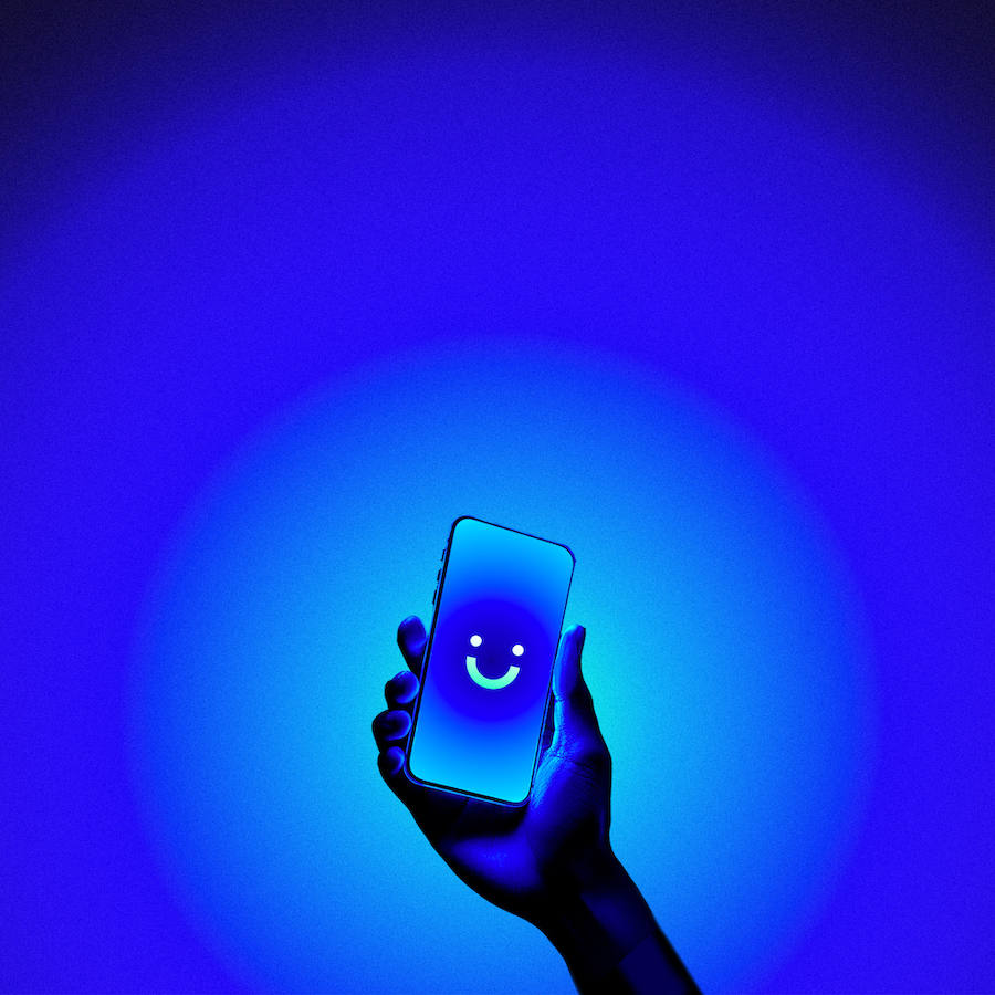 Hand holding a smartphone displaying a glowing blue screen with a smiling face icon, set against a radiant blue background.