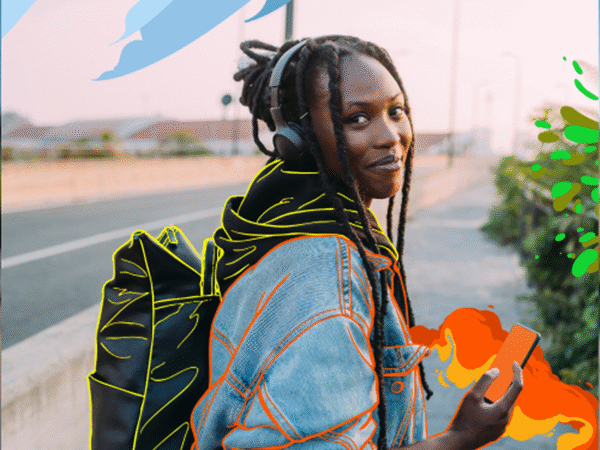 Young person with dreadlocks wearing headphones and a denim jacket outlined with bright colors, carrying a black backpack also outlined, holding a smartphone with fiery orange-red digital effects, standing on a sidewalk next to a road at sunset.