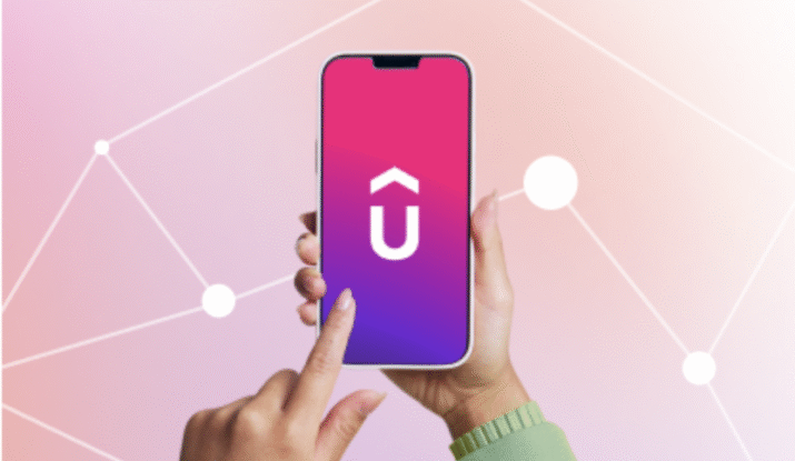 A hand holding a smartphone showing a pink and purple gradient screen with a white uppercase letter U topped by a circumflex accent, while another hand is about to tap the screen, with a pink and white geometric network background.