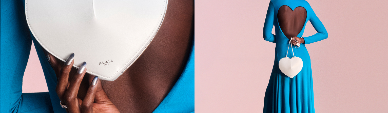 Close-up of a person in a blue dress with a heart-shaped open back holding a white heart-shaped bag with the brand name Alaïa Paris on it against a pink background