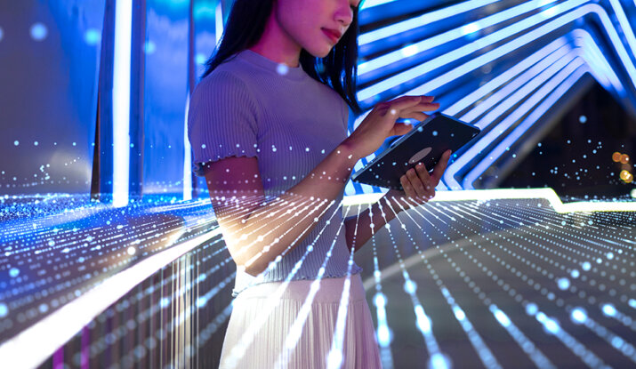 Young woman using a tablet in a futuristic setting with blue neon lights and digital data lines projected around her.