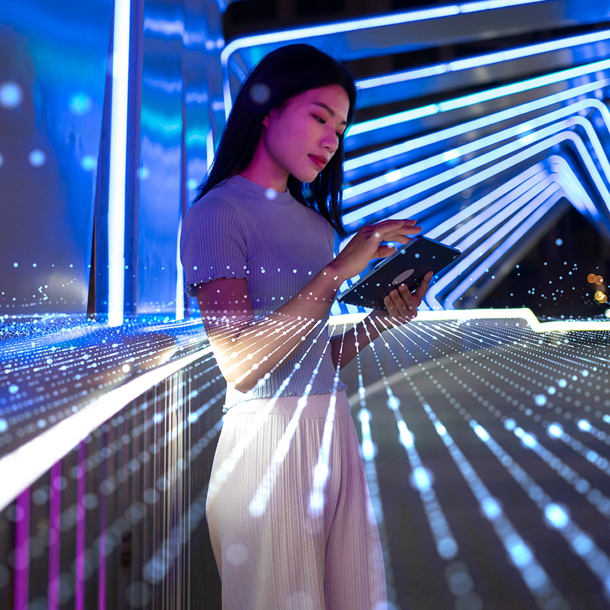 Young woman using a tablet in a futuristic setting with blue neon lights and digital data lines projected around her.