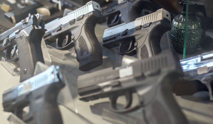 Various handguns displayed on clear stands inside a glass case with a green grenade-like object in the background.
