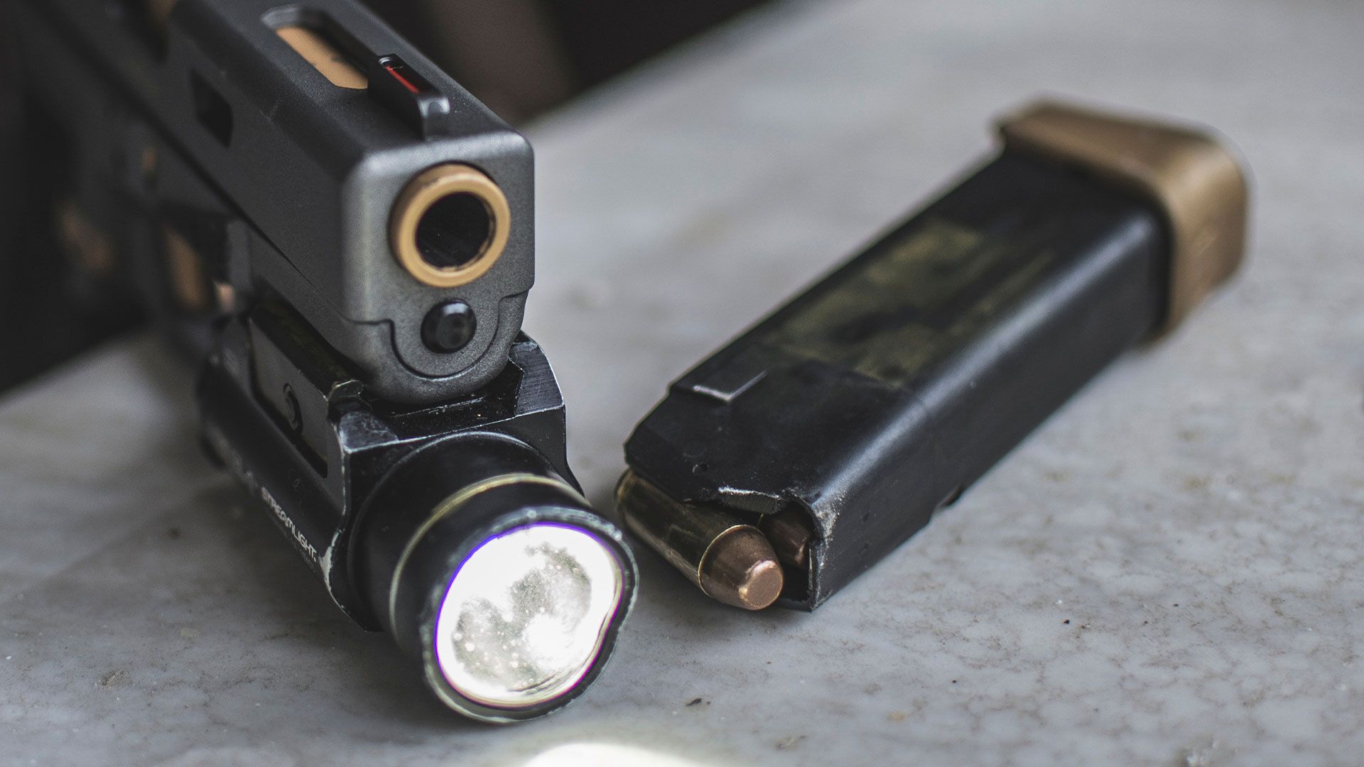 Close-up view of a handgun with a tactical flashlight attached and a loaded magazine placed next to it on a marble surface.