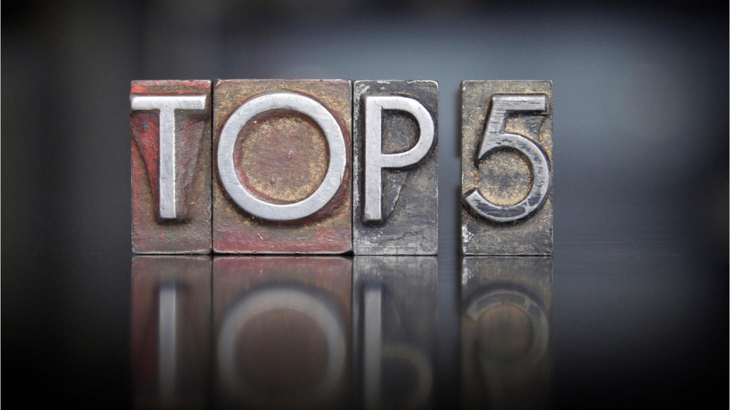 Metal letterpress blocks spelling out the phrase 'TOP 5' with a reflective surface underneath and a blurred, dark background.