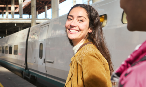 Smiling woman with suitcase standing by train platform