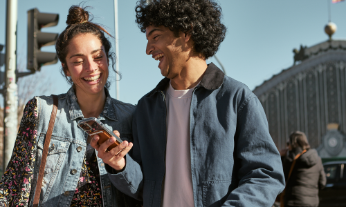 Young couple smiling and looking at phone outdoors