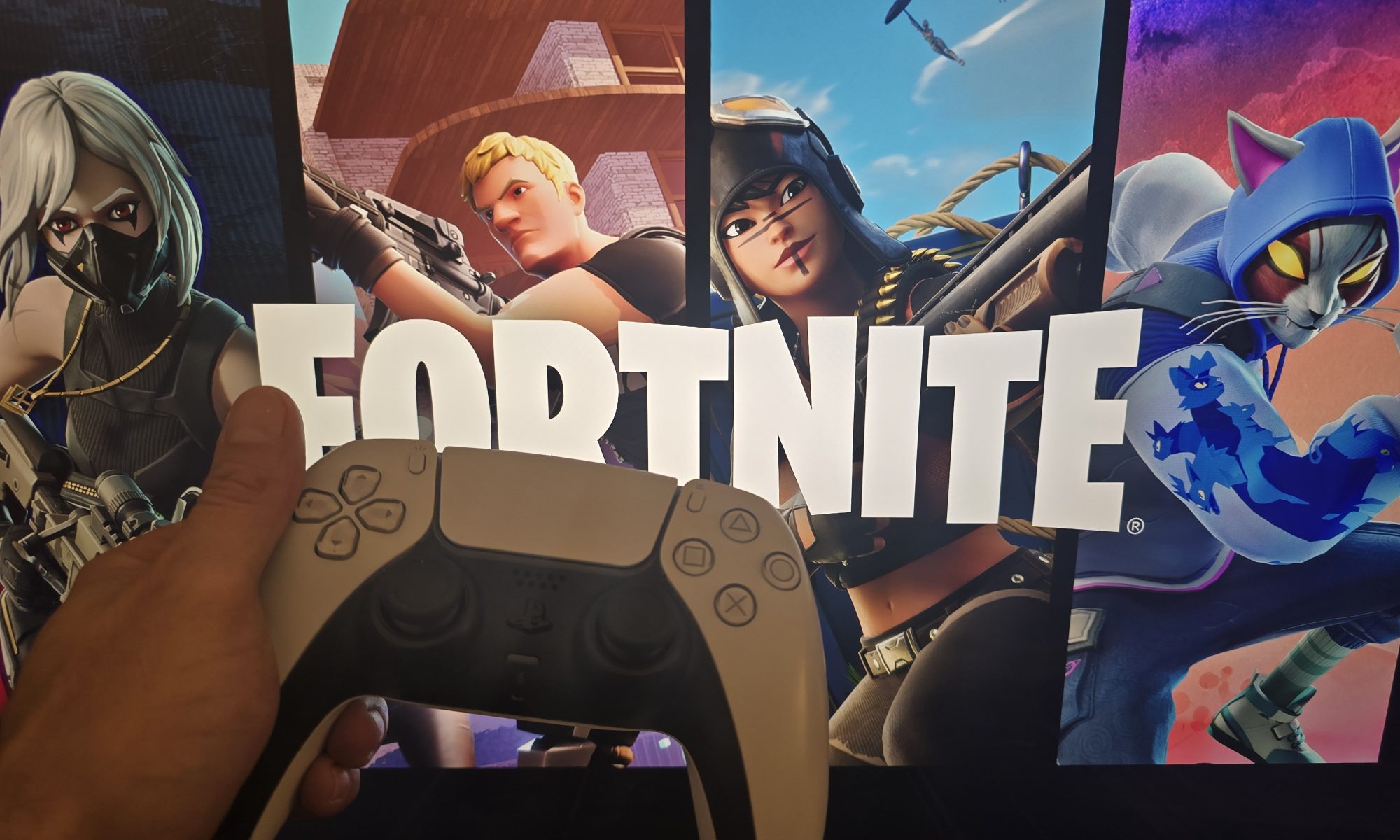 Hand holding PlayStation controller in front of Fortnite game screen